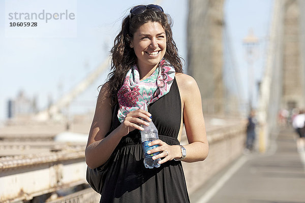 Frau hält Wasserflasche mit Brooklyn Bridge im Hintergrund