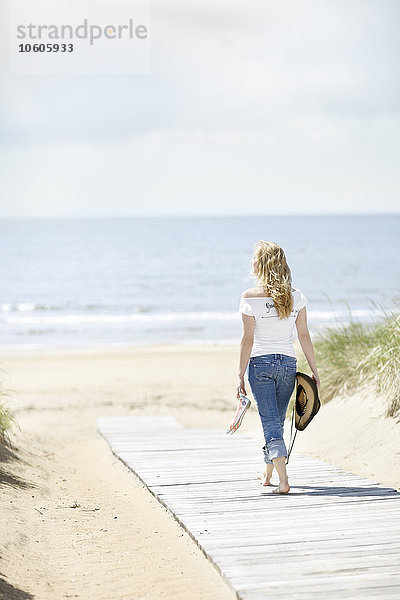 Junge Frau geht am Strand mit Meer im Hintergrund