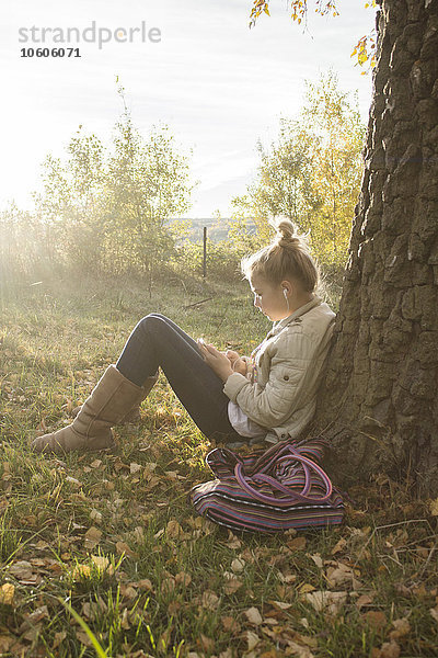 Mädchen sitzt unter einem Baum und hört Musik