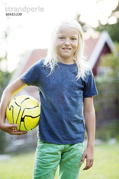 Porträt eines Jungen mit langen  blonden Haaren  der einen Ball hält