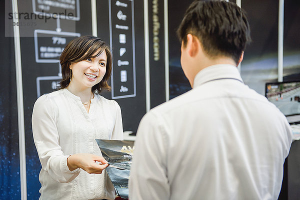 Junge attraktive japanische Geschäftsfrau unterhält Kunden am Messestand