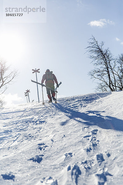 Mann trägt Skier einen verschneiten Hang hinauf
