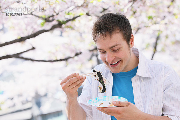 Kaukasischer Mann isst Sushi mit Stäbchen während der Hanami-Saison