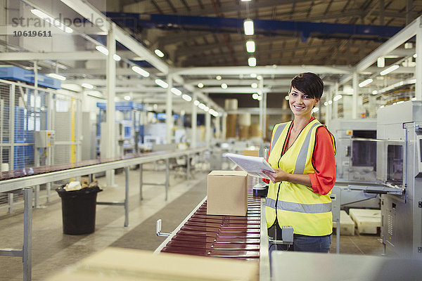 Portrait lächelnder Arbeiter beim Kontrollieren von Kartons auf der Förderband-Produktionslinie in der Fabrik