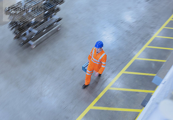 Arbeiter in reflektierender Kleidung mit Werkzeugkasten in der Fabrik