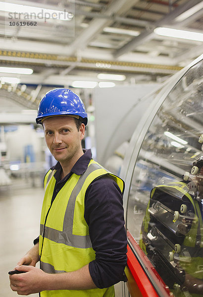Porträt eines selbstbewussten Arbeiters  der sich auf Maschinen in der Fabrik stützt.