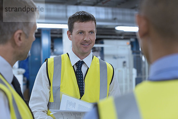 Arbeiter in reflektierender Kleidung sprechen in der Fabrik