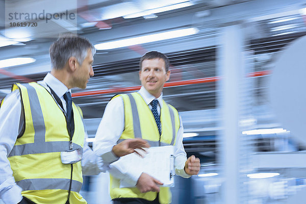 Geschäftsleute in reflektierender Kleidung gehen und reden in der Fabrik