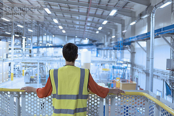 Arbeiter in reflektierender Kleidung auf Plattform mit Blick über die Fabrik