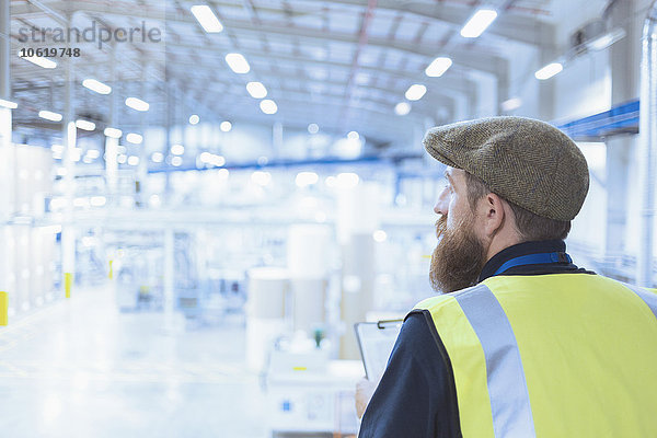 Arbeiter mit Bart und Baskenmütze mit Blick über die Fabrik