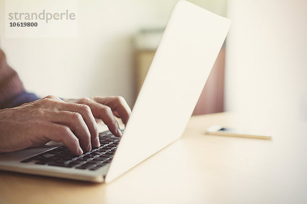 Senior Mann beim Tippen auf dem Laptop am Tisch