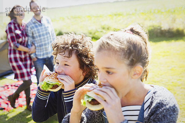 Geschwister essen Hamburger auf dem sonnigen Campingplatz