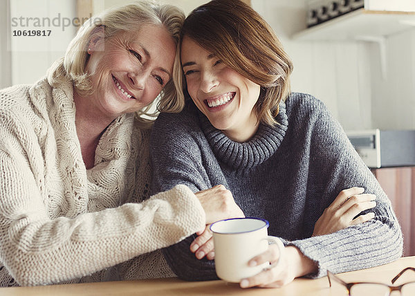 Lachende Mutter und Tochter in Pullovern umarmend und Kaffee trinkend