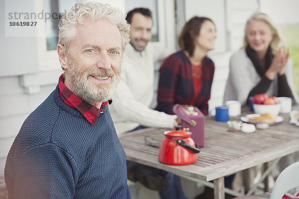 Portrait lächelnder älterer Mann beim Frühstück mit der Familie auf der Terrasse