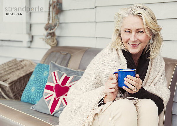 Portrait lächelnde Seniorin beim Kaffeetrinken auf dem Terrassensofa