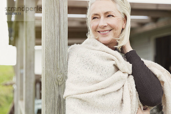 Lächelnde Seniorin mit Schal auf der Veranda