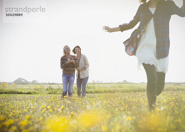 Frauen beobachten Mädchen beim Laufen auf einer sonnigen Wiese mit Wildblumen