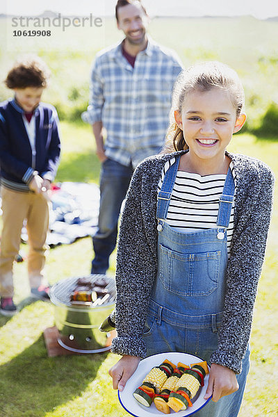 Portrait lächelndes Mädchen mit Gemüsespießen auf dem sonnigen Campingplatz