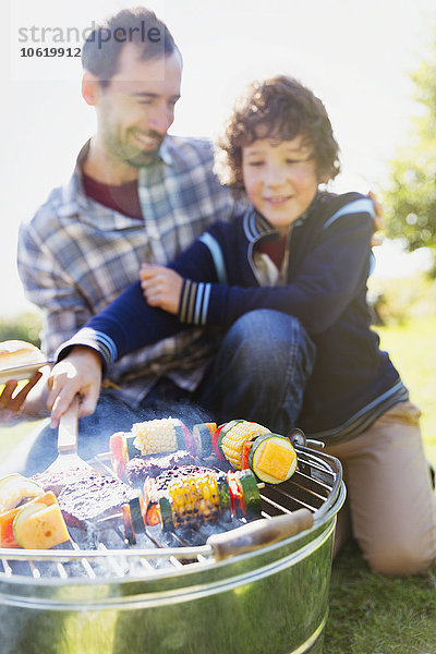 Vater und Sohn grillen Hamburger und Gemüsespieße