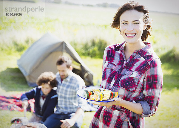 Portrait lächelnde Frau mit Gemüsespießen auf dem sonnigen Campingplatz