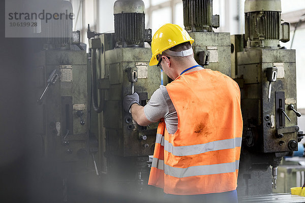 Arbeiter in Arbeitsschutzbekleidung  der Maschinen in der Fabrik betreibt