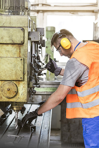 Arbeiter in Arbeitsschutzbekleidung  der Maschinen in der Fabrik betreibt