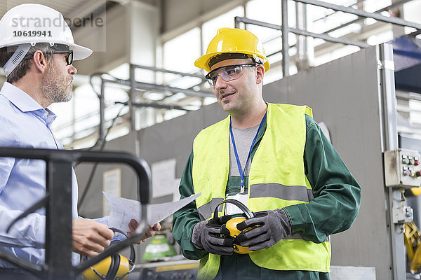 Ingenieur und Arbeiter in Arbeitsschutzkleidung im Gespräch in der Fabrik