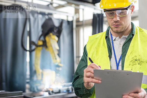 Arbeiter in Arbeitsschutzkleidung mit Klemmbrett im Werk