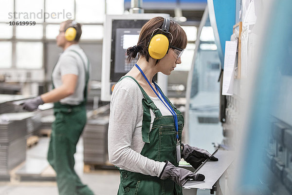 Arbeiterin mit Gehörschutz  die das Metallteil in der Fabrik hält