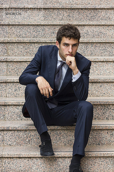 Porträt eines jungen Geschäftsmannes auf der Treppe mit der Hand am Kinn