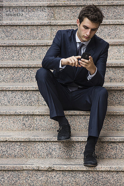 Portrait eines jungen Geschäftsmannes auf einer Treppe mit dem Smartphone