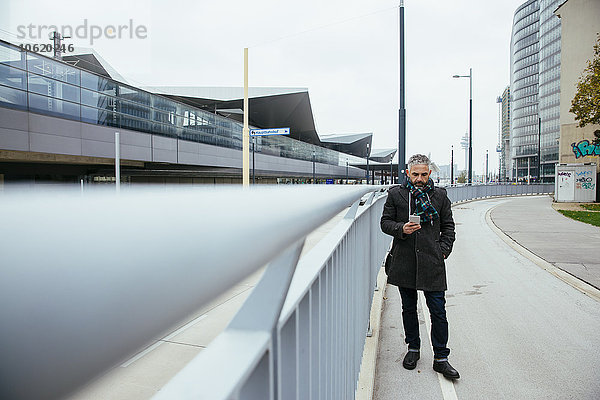 Österreich  Wien  Mann auf einer Gasse in der Nähe des Hauptbahnhofs mit Blick auf sein Smartphone
