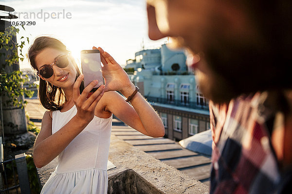 Österreich  Wien  lächelnde junge Frau beim Fotografieren ihres Freundes auf einer Dachterrasse