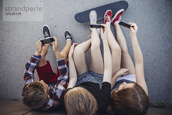 Drei Teenager im Freien mit Smartphones und Skateboard