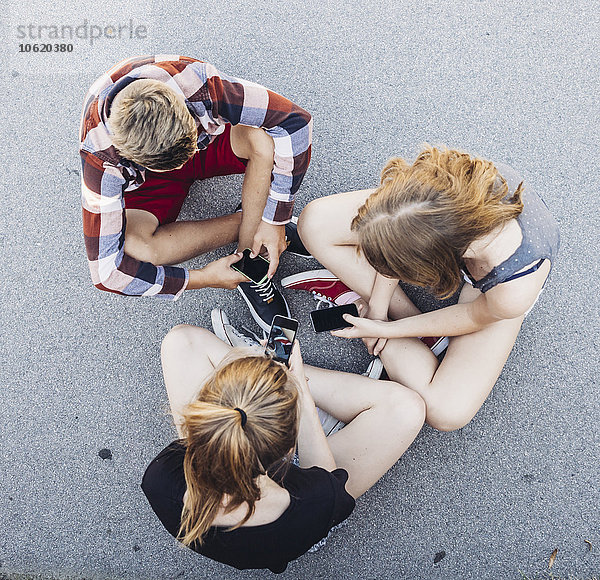 Drei Teenager sitzen im Freien mit Smartphones