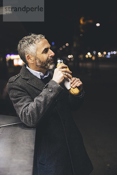 Österreich  Wien  Mann mit Käse Carniolan Wurst am Wurststand bei Nacht