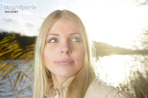 Porträt einer blonden Frau vor einem See im Gegenlicht