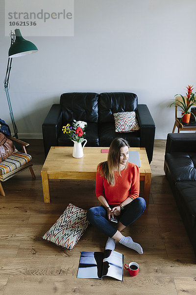 Junge Frau sitzt auf dem Boden ihres Wohnzimmers und entspannt sich.