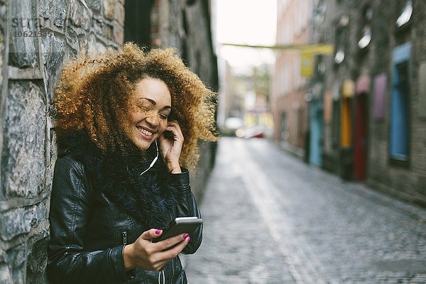 Irland  Dublin  lächelnde Frau mit Afro-Hörmusik mit Smartphone und Kopfhörer