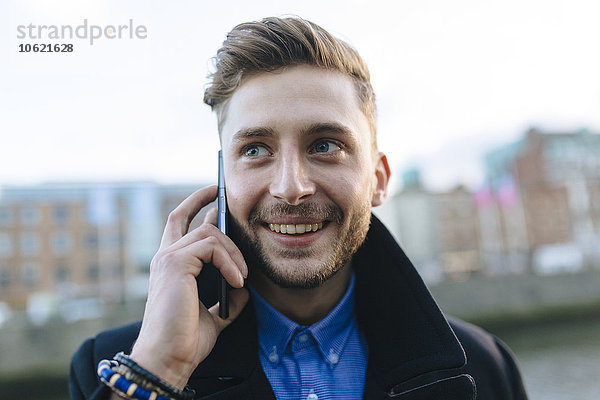 Irland  Dublin  Portrait eines lächelnden jungen Geschäftsmannes beim Telefonieren mit Smartphone