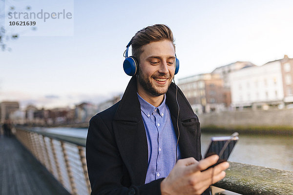 Irland  Dublin  junger Mann mit Smartphone  der Musik mit Kopfhörern hört.
