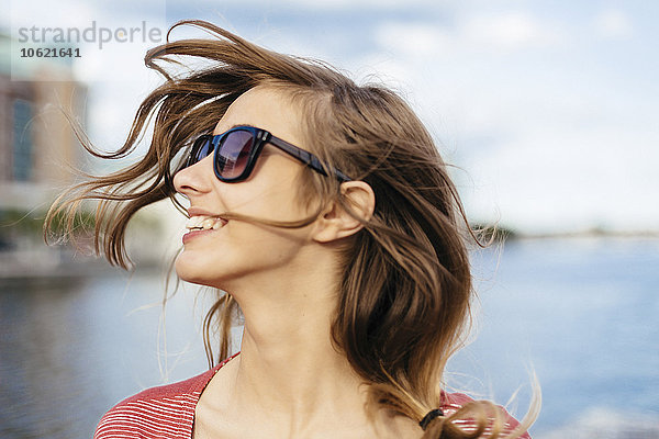 Porträt einer lächelnden Frau mit blasenden Haaren und Sonnenbrille