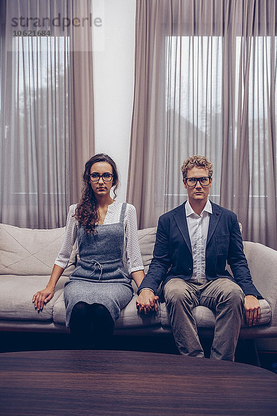 Junges Paar zu Hause auf dem Sofa sitzend mit leerem Gesichtsausdruck