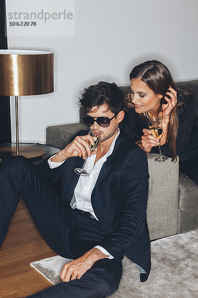 Stilvolles junges Paar mit Gläsern Champagner auf dem Sofa