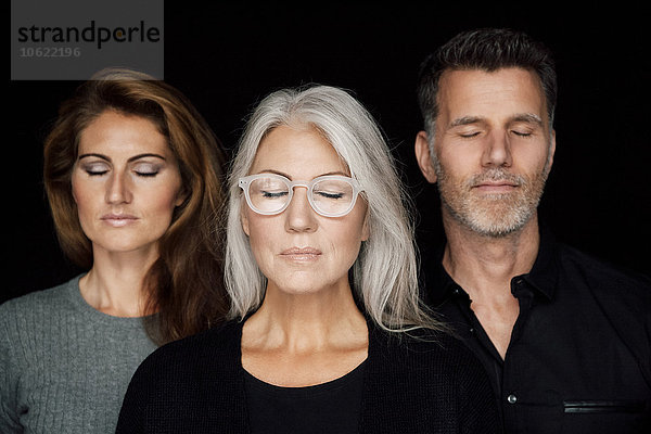 Porträt von drei Personen mit geschlossenen Augen vor schwarzem Hintergrund