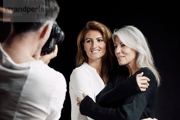 Mann fotografiert zwei Frauen vor schwarzem Hintergrund