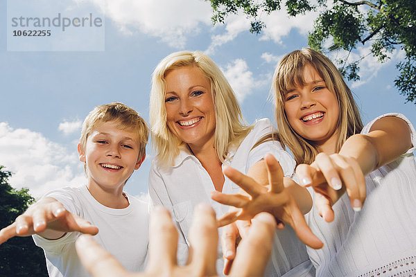 Porträt der glücklichen Mutter mit ihren Kindern  die nach der Hand des Fotografen greifen.
