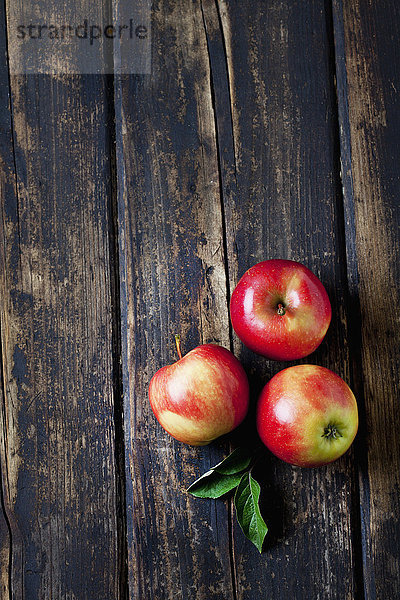 Drei rote Äpfel und Blätter auf dunklem Holz