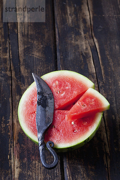 Hälfte und Stück Mini-Wassermelone und Messer auf dunklem Holz