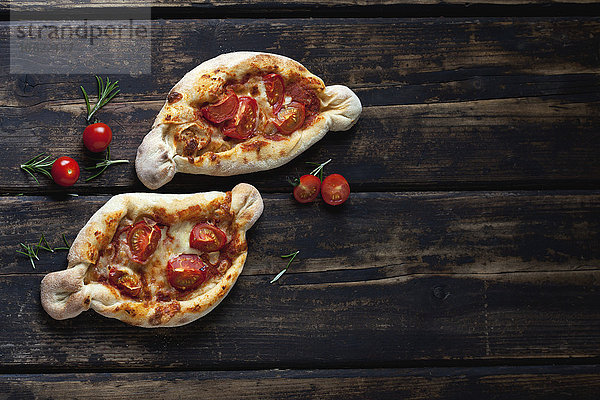 Zwei kleine Pizzen  Rosmarin und Kirschtomaten auf dunklem Holz